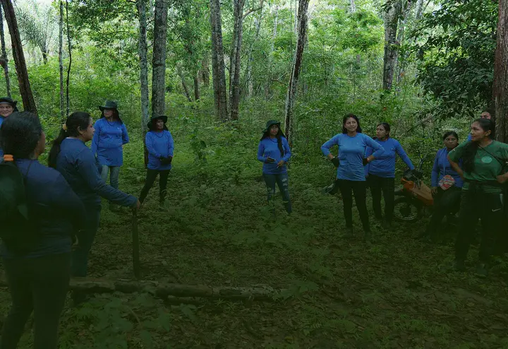 Mulheres indígenas reunidas em roda na floresta.